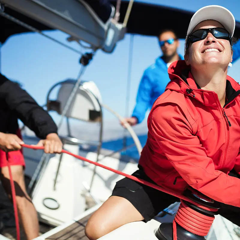Tre persone al lavoro su una barca a vela; in primo piano una donna al verricello con una cima rossa