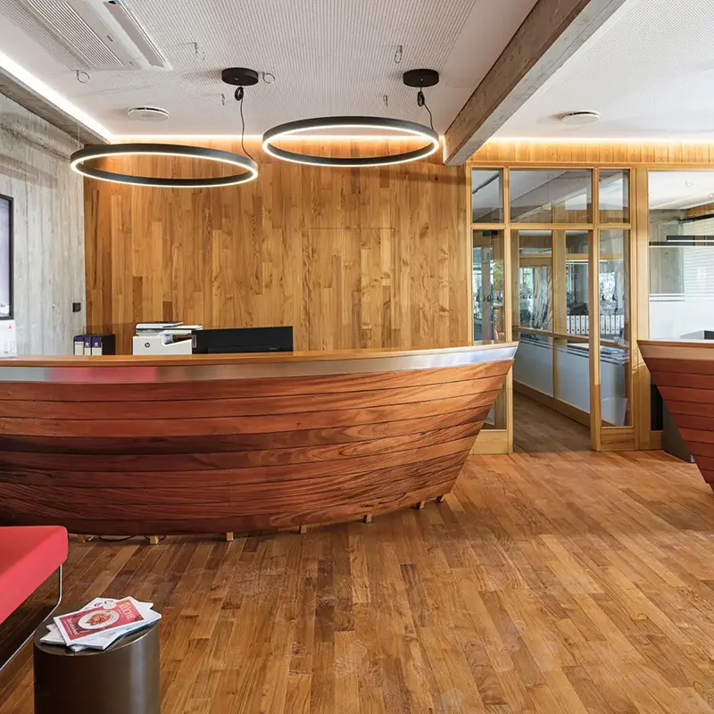 Reception con un bancone in legno a forma di scafo, pareti rivestite in legno e lampade circolari